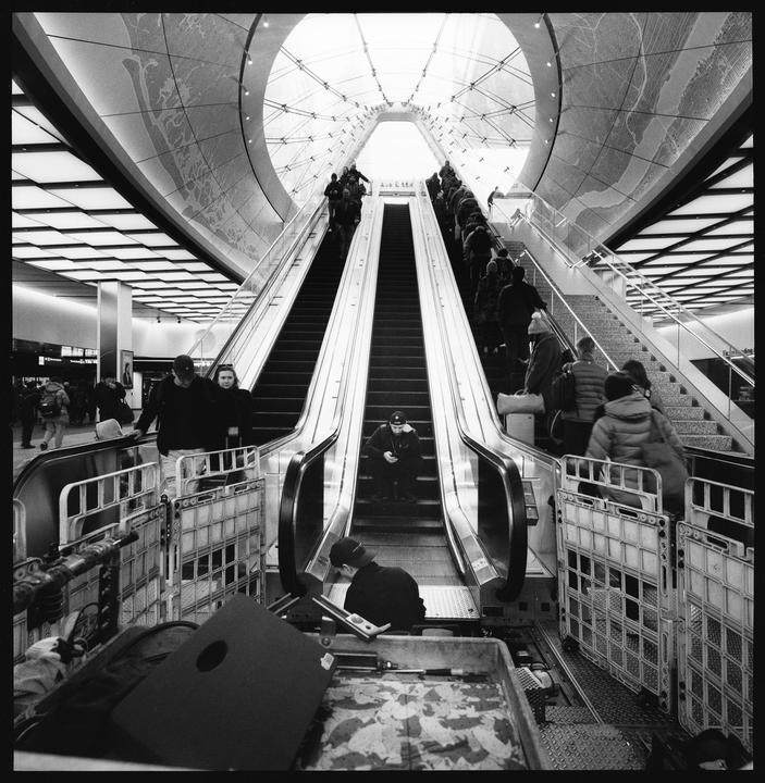People ride escalators and stairs in a large, modern building with a glass ceiling.