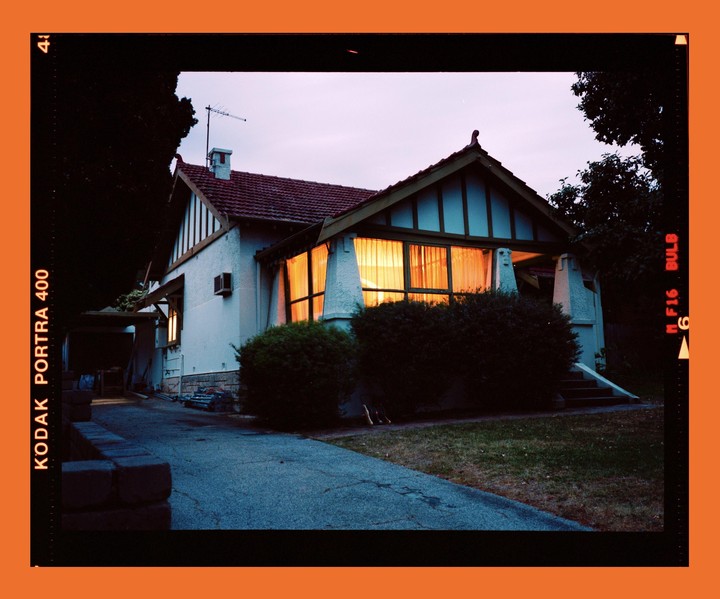 A house with illuminated windows is seen from a driveway at dusk.