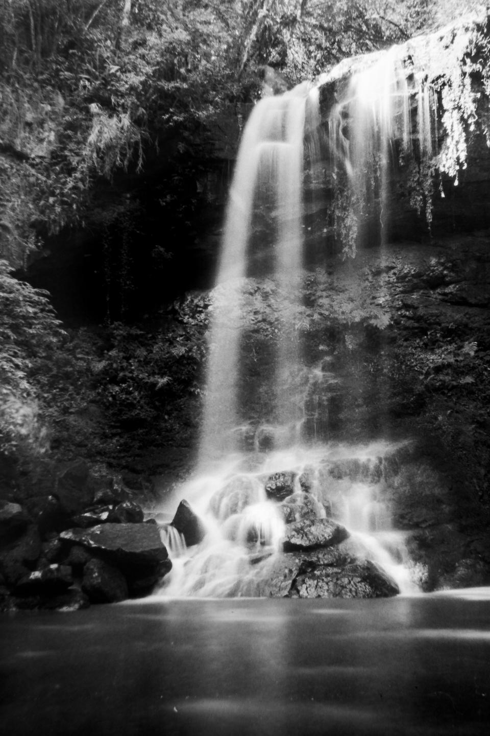 A waterfall cascades over rocks into a pool of water surrounded by lush vegetation.