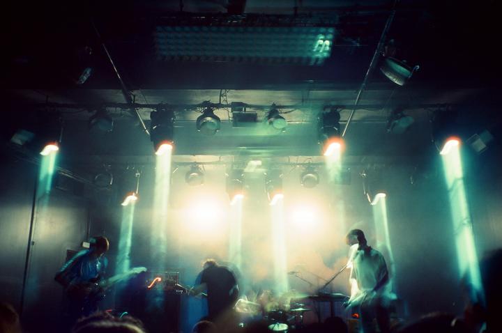 A band performs on a stage illuminated by bright spotlights and hazy light.