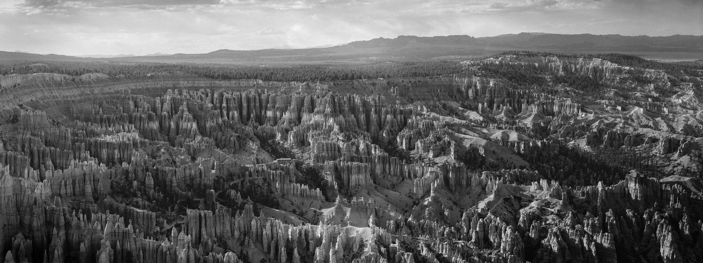 A panoramic view shows the vast landscape of Bryce Canyon with its unique rock formations under a cloudy sky.