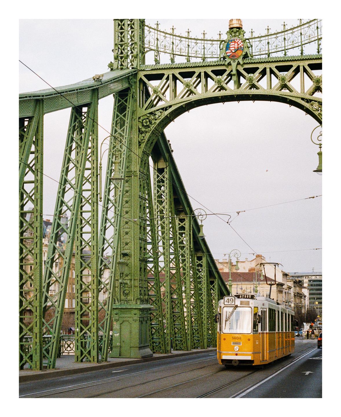 A yellow tram crosses the green metal Liberty Bridge in Budapest.