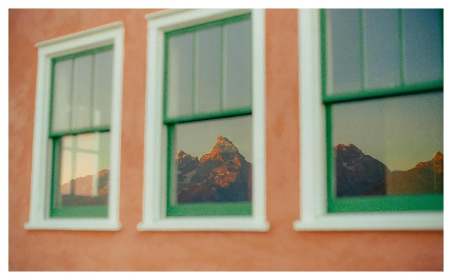 Three windows with green frames reflect a mountain range under a sunrise sky.