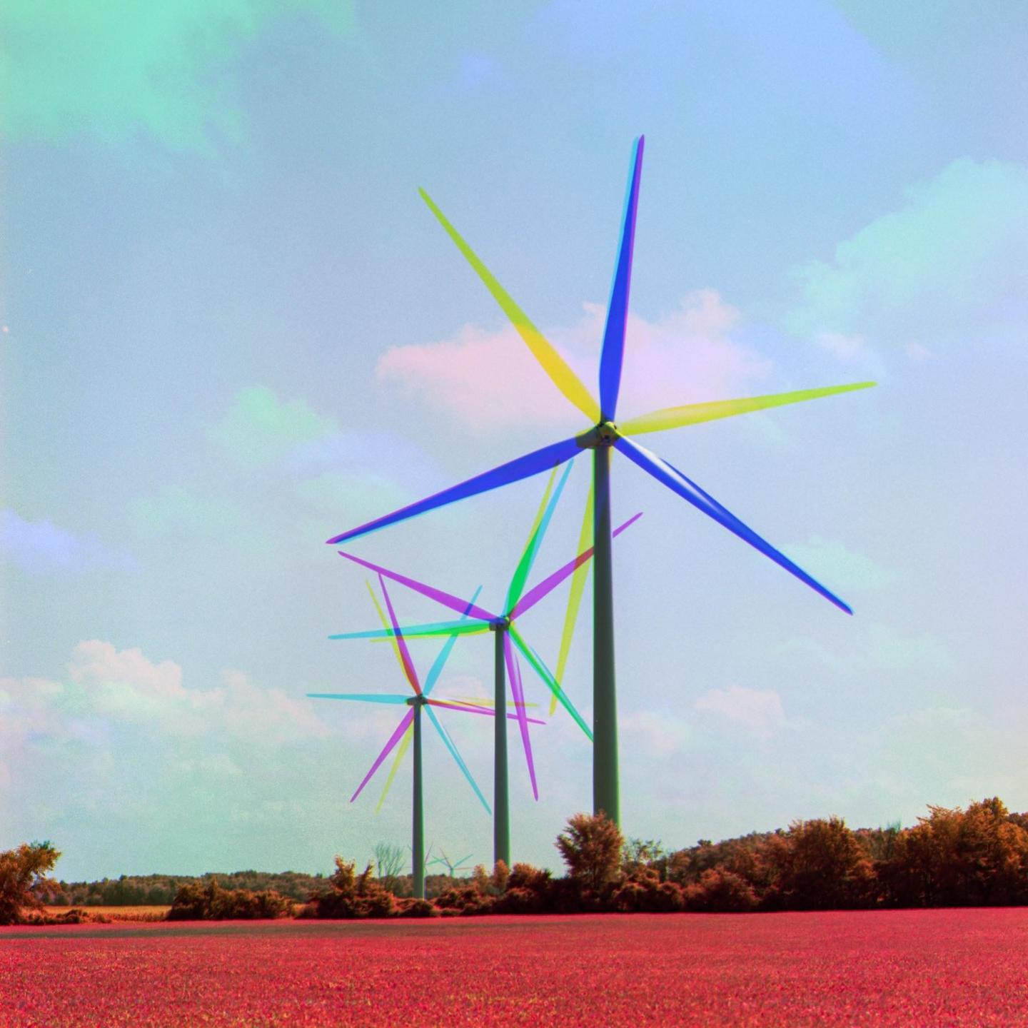 Three wind turbines with colorful blades stand in a red field under a blue sky with clouds.