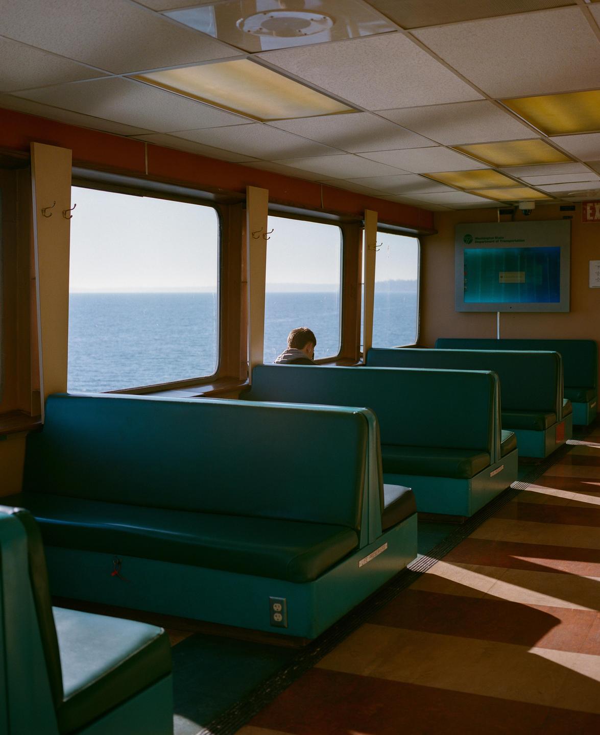 A person sits on a ferry looking out at the water through a window.