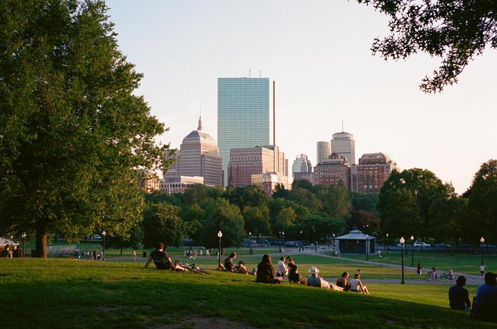 People relax on a grassy hill with a city skyline in the background.