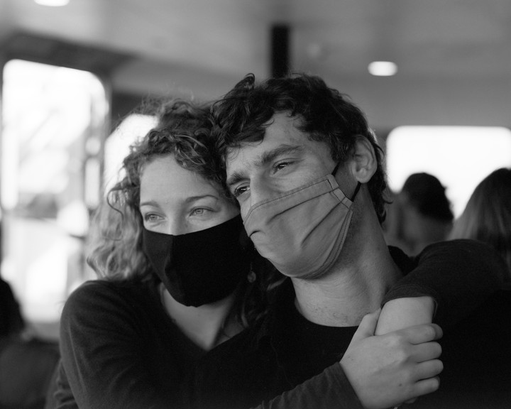 A couple wearing face masks embraces and looks into the distance.