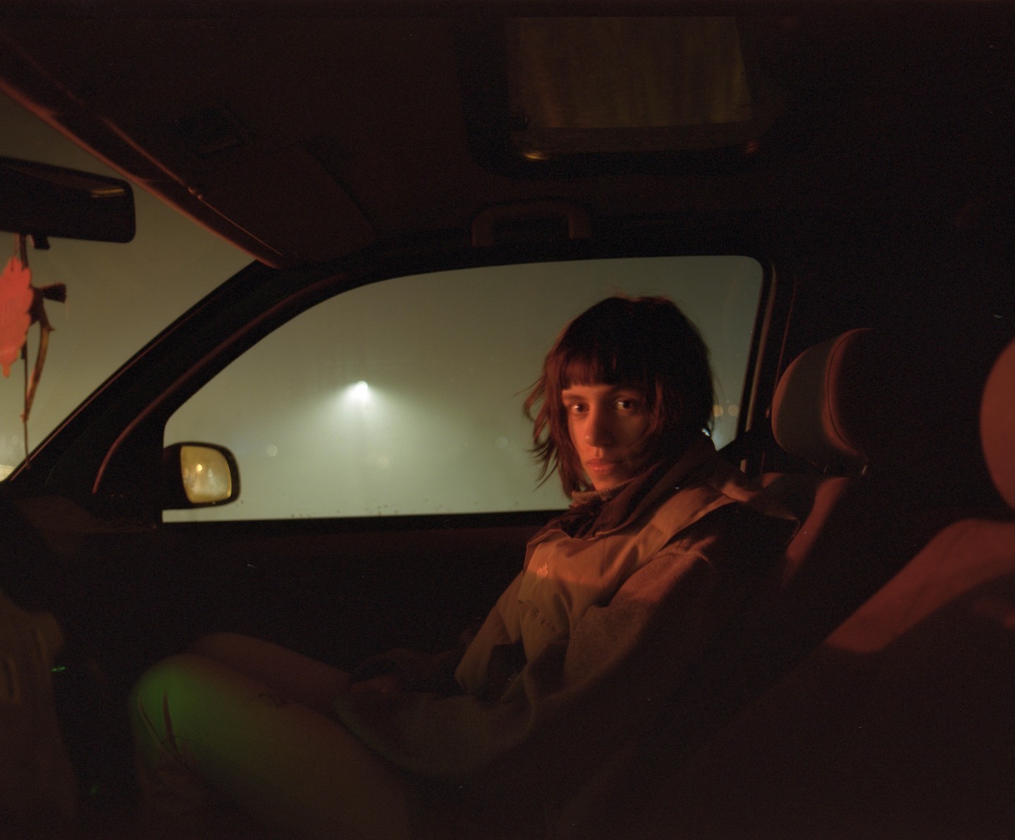 A woman sits in a car at night, looking towards the viewer.