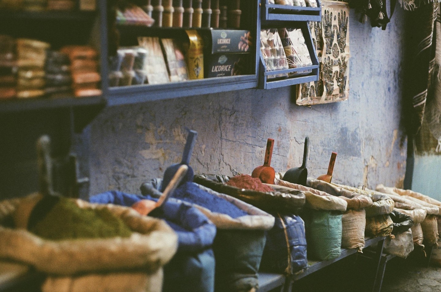 Bags of colorful paint pigment with scoops are arranged on a shelf below other items in a shop.
