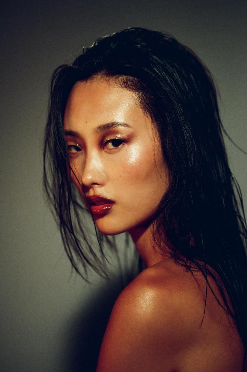 A woman with dark hair and glossy red lips looks over her shoulder at the viewer.