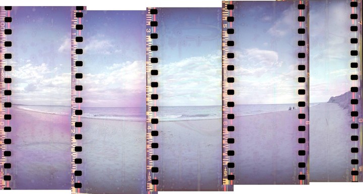 A panoramic view of a beach with waves crashing on the shore under a cloudy sky, with film sprockets visible on the edges.