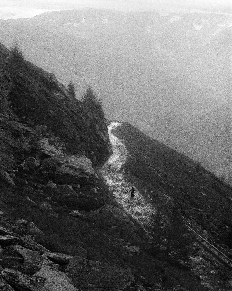 A person rides a bicycle on a winding mountain path on a hazy day.