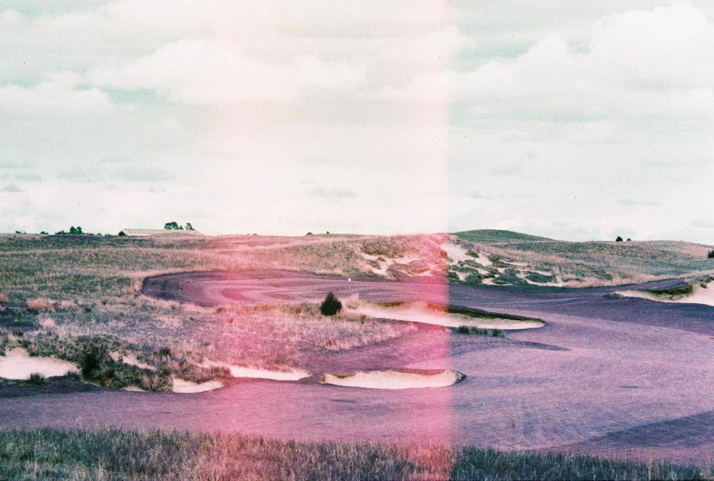 A golf course with sand traps and hills in the background is visible under a cloudy sky.