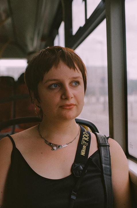 A woman with short hair and a necklace looks out a bus window.