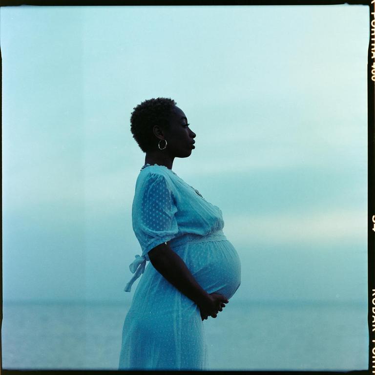 A pregnant woman in a white dress stands in profile against a blue background.