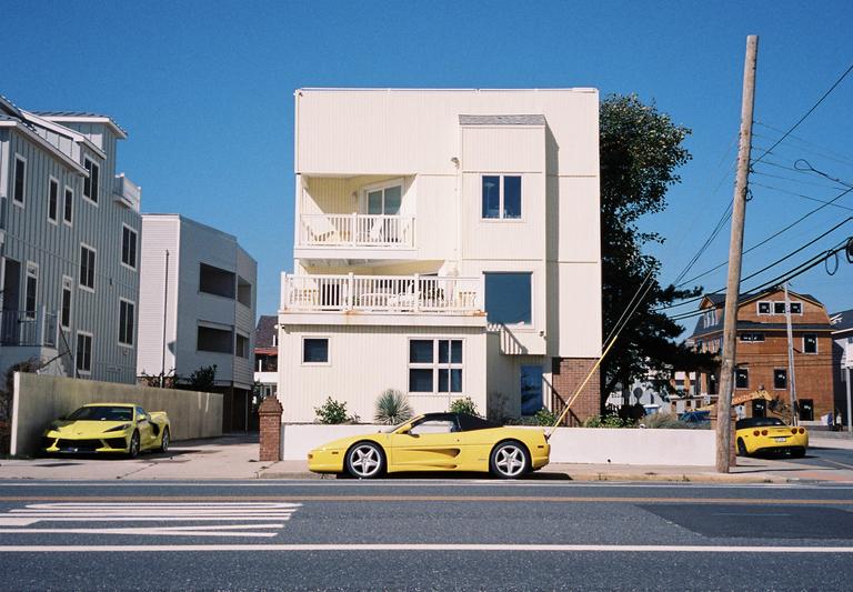 Three yellow sports cars are parked on a street in front of houses on a clear day.