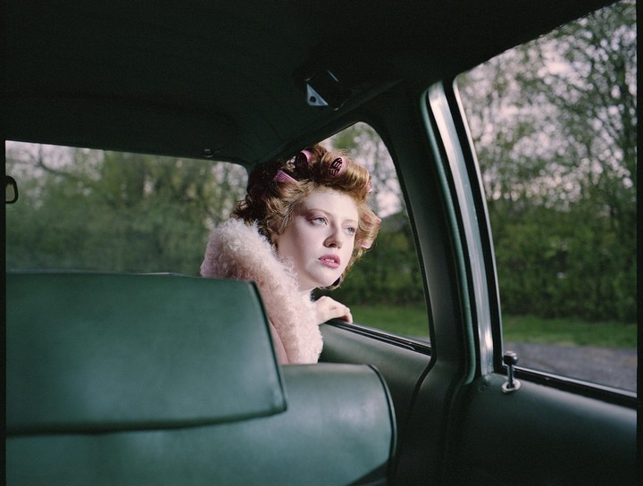 A woman with hair curlers looks out the window of a car.