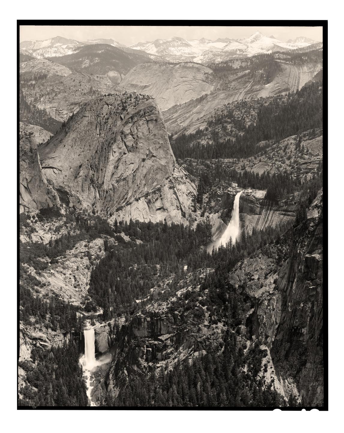 A black and white landscape shows a valley with two waterfalls, surrounded by mountains and pine trees.