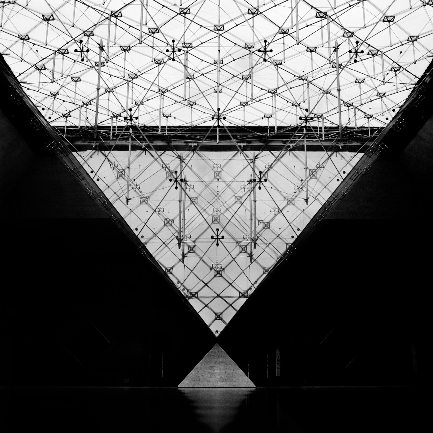 A small pyramid sits below a large glass pyramid with a grid pattern.
