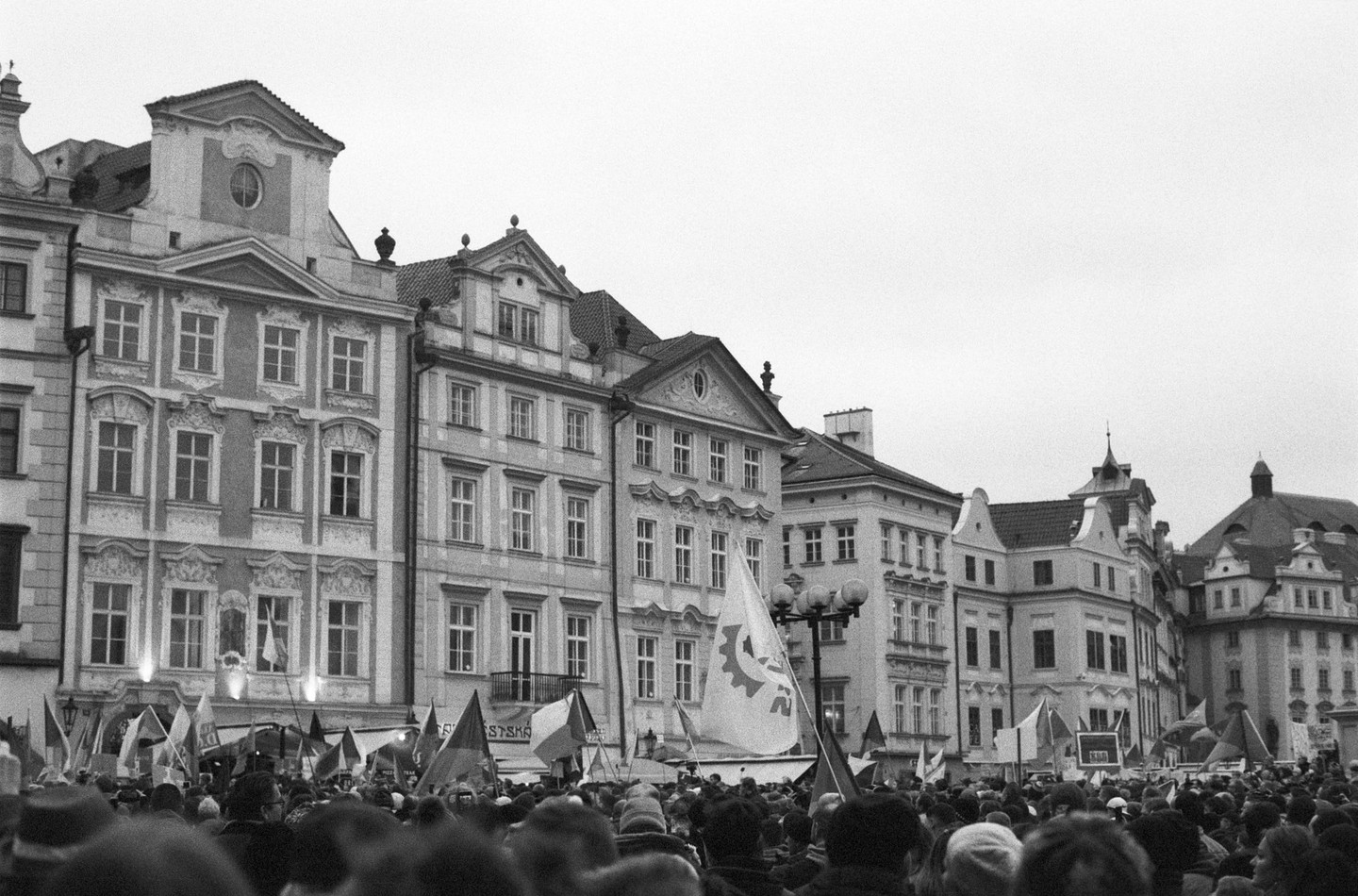 A large crowd of people with flags stands in front of ornate buildings in Prague.