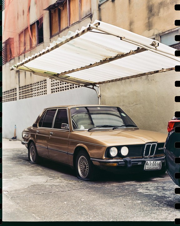A gold sedan with a flat tire is parked under a white awning next to a building.