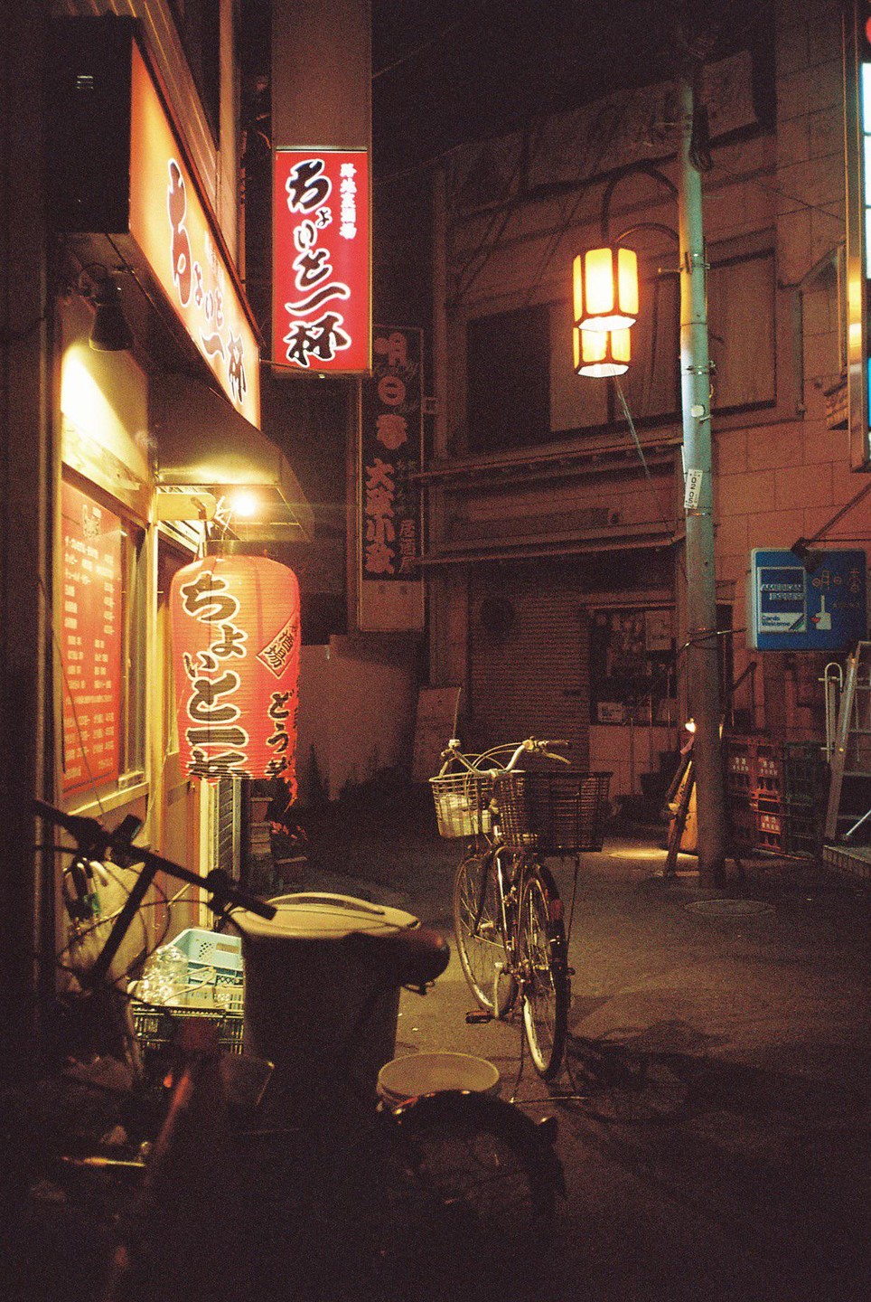 A bicycle is parked on a street at night next to a building with illuminated signs and a red lantern.