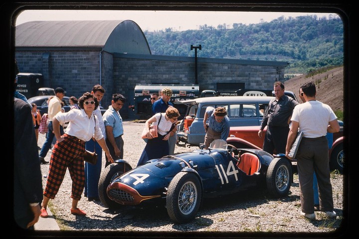 A group of people are gathered around a race car with the number 114 on its side.