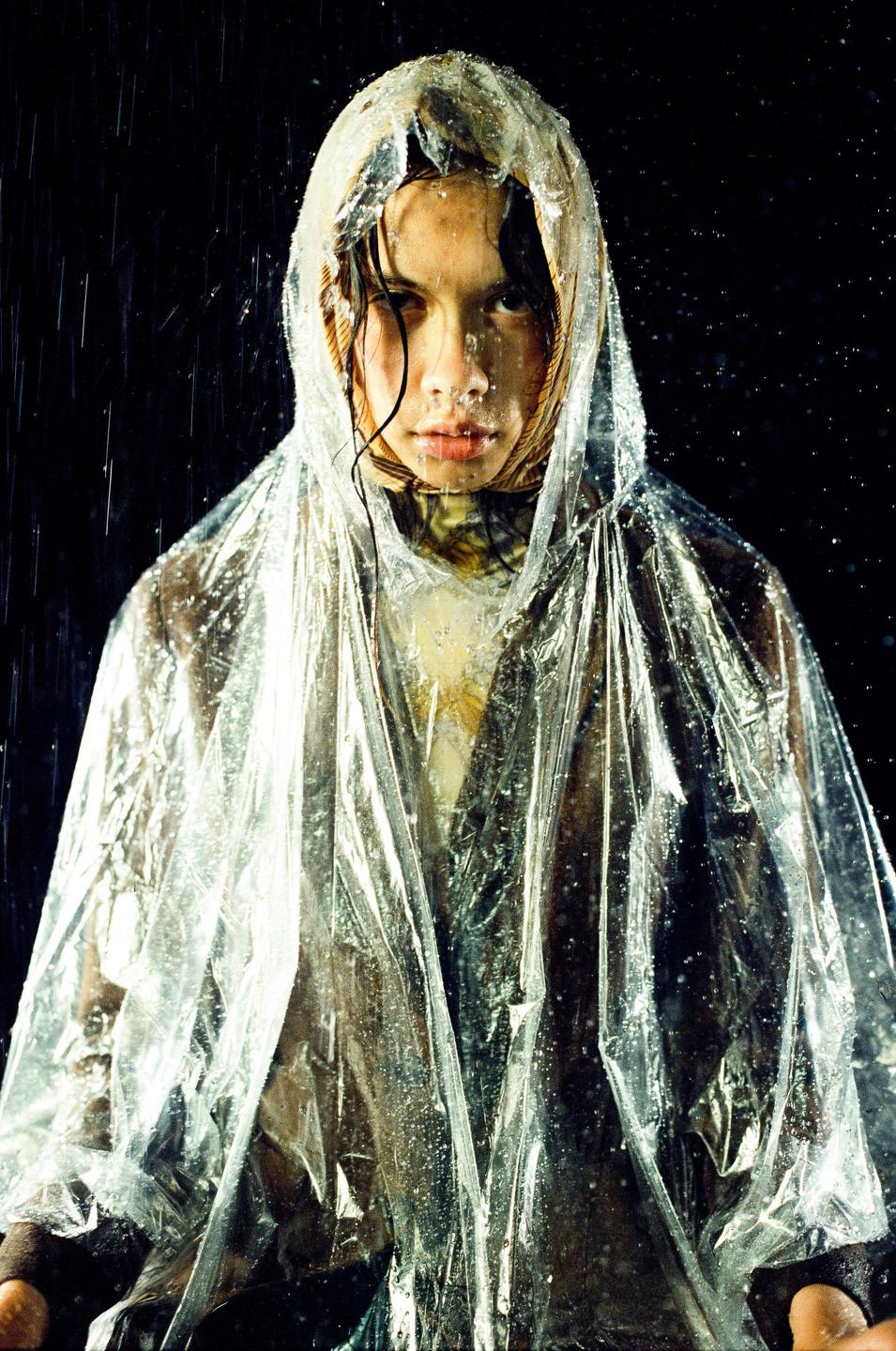 A woman wearing a clear plastic poncho stands in the rain at night.