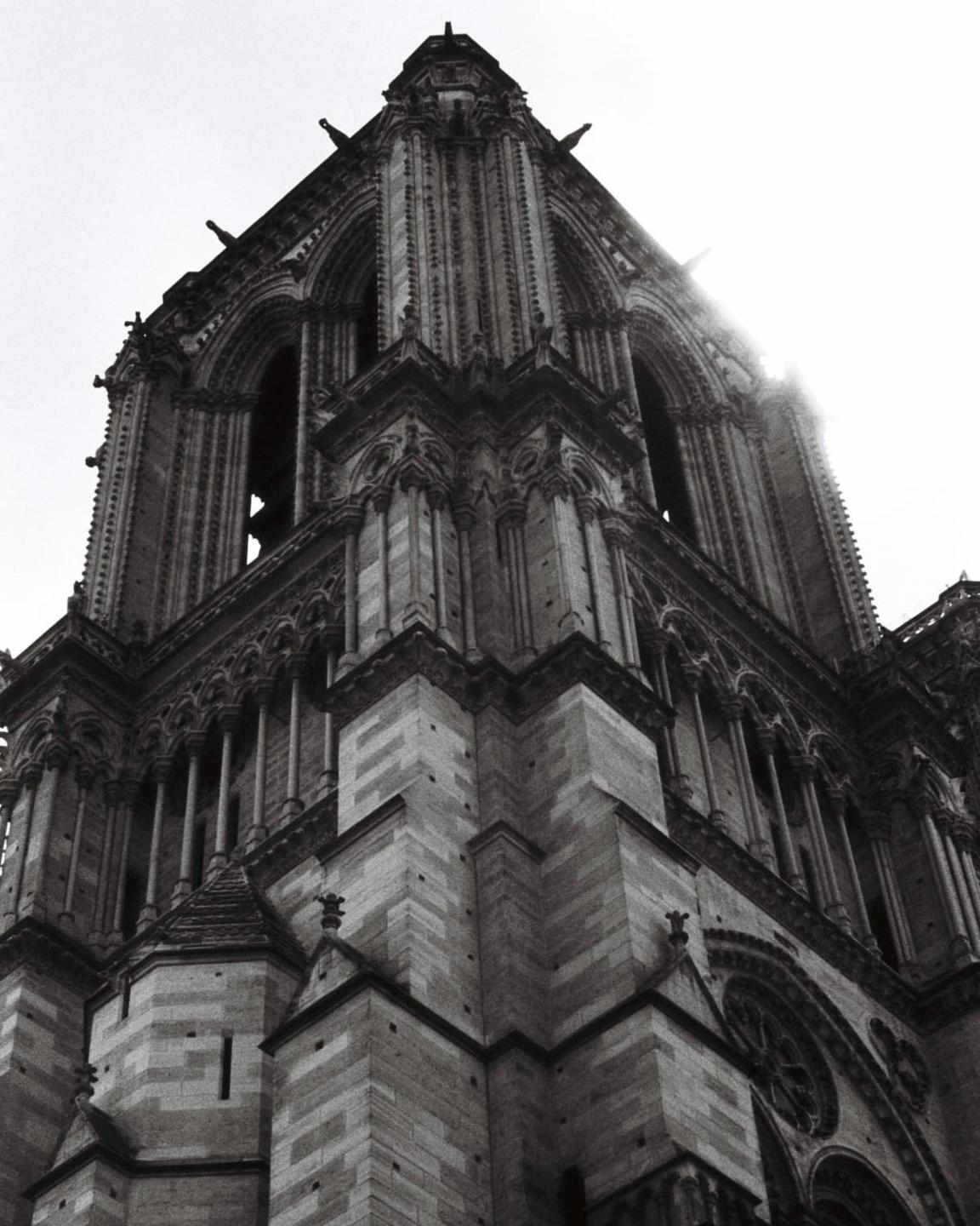 The corner of a gothic cathedral tower is seen from below, with light shining through the arches.