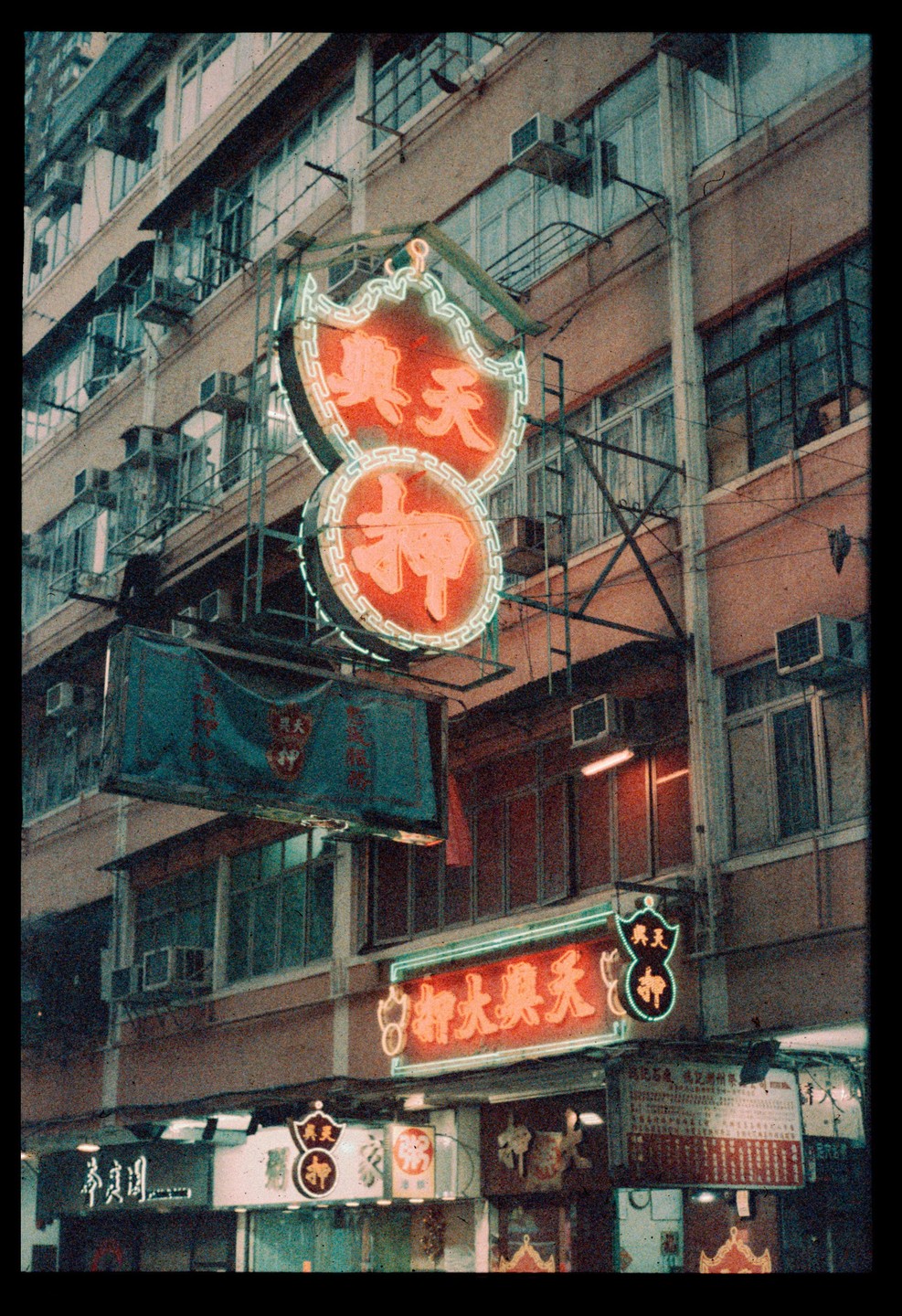 A building facade is covered in neon signs and air conditioning units at night.