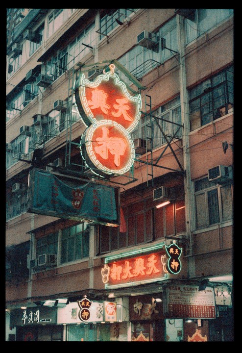 A building facade is covered in neon signs and air conditioning units at night.