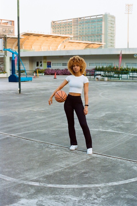 A woman with curly hair stands on a basketball court holding a basketball.