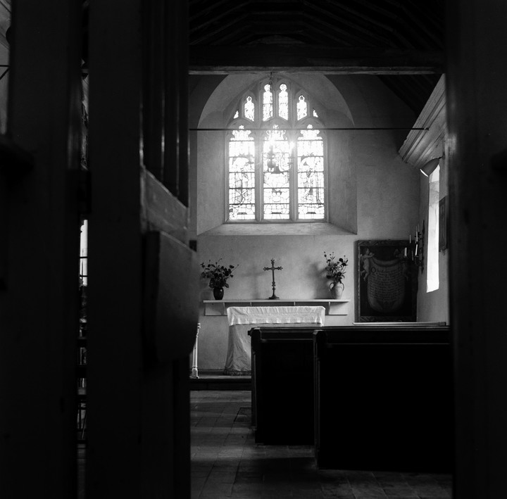 A black and white image shows the interior of a church with a large stained glass window at the back.