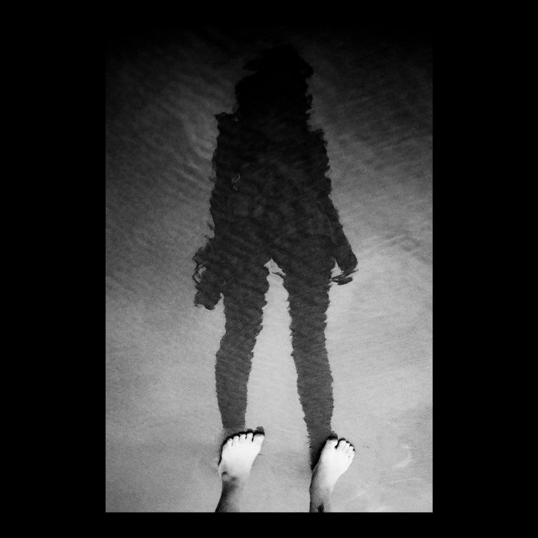 A person's feet are visible at the bottom of the frame, with their shadow reflected in the water above them.
