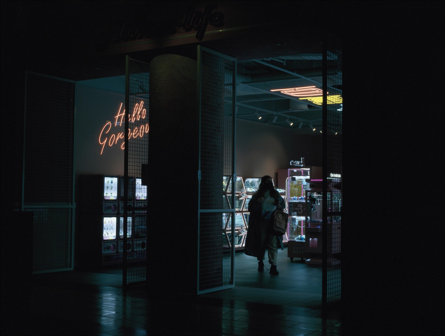 A woman walks into a store with a neon "Hello Gorgeous" sign on the wall.