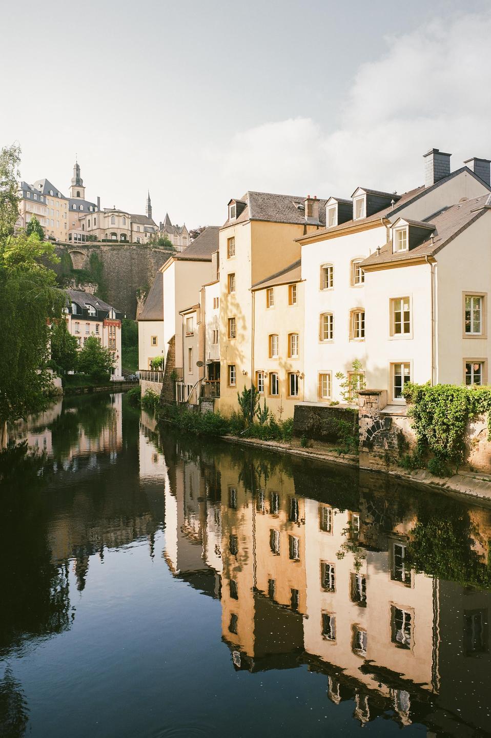 Buildings with reflections in a river are visible in the Grund district of Luxembourg.