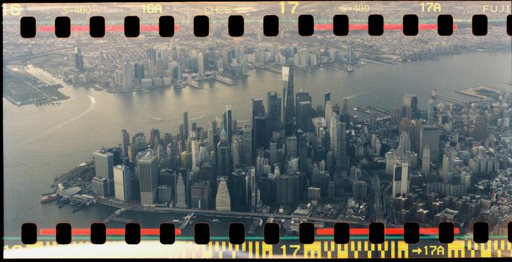 An aerial view shows a dense urban landscape with numerous skyscrapers and a wide river.