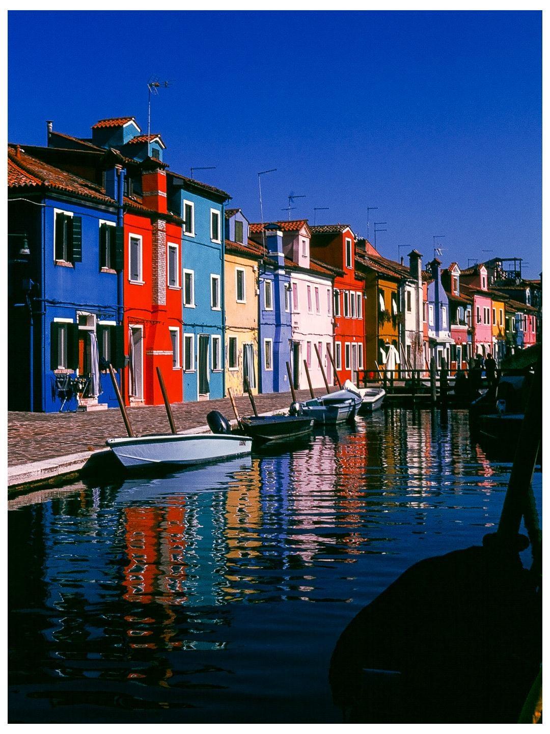 A canal with colorful houses and boats is visible under a clear blue sky.