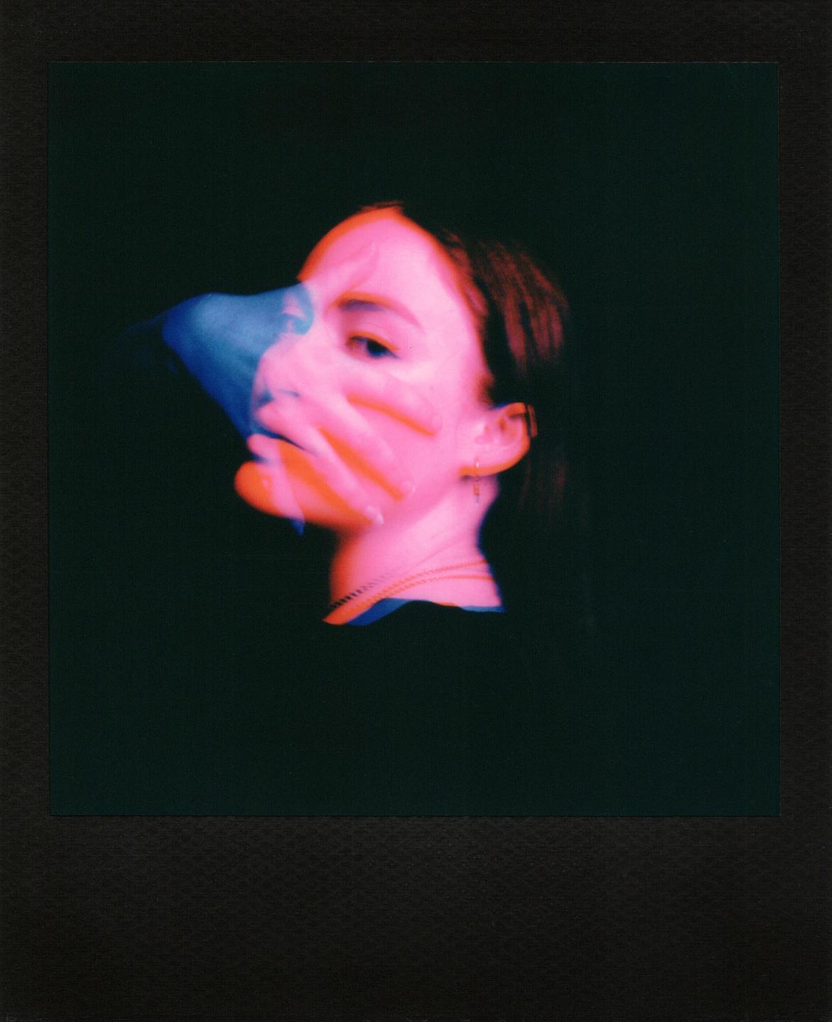 A woman's face is visible in a double exposure with a hand in front of her face.