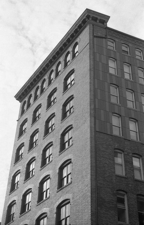 A tall building with many windows is shown from a low angle, with one side in shadow and the other illuminated.