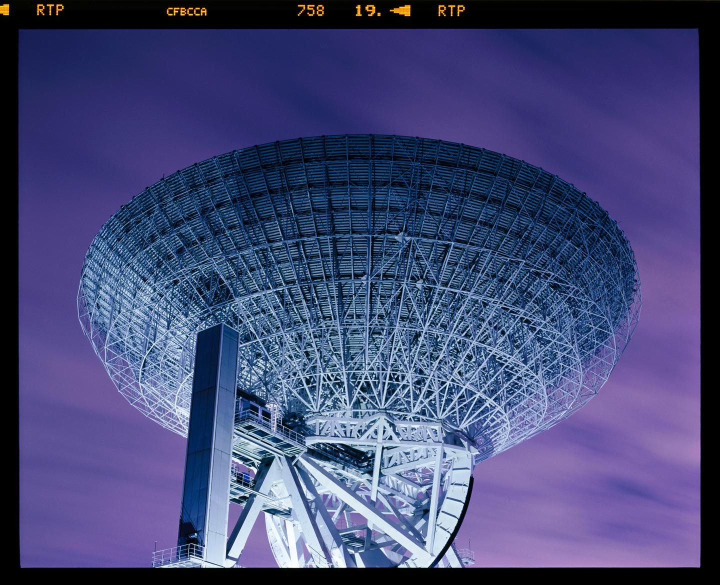 A large satellite dish is angled towards a purple sky.