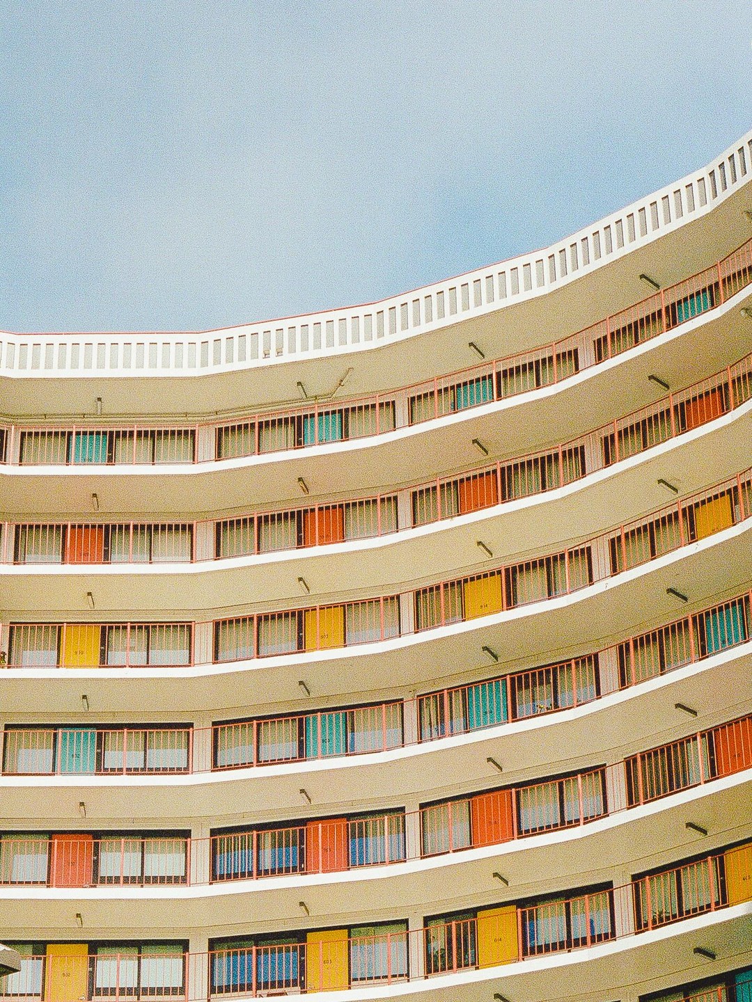 A curved building with many balconies and colorful doors is shown from a low angle.