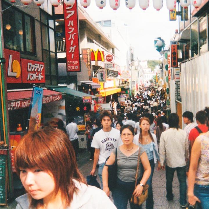 A crowd of people walk down a narrow street lined with shops and signs.