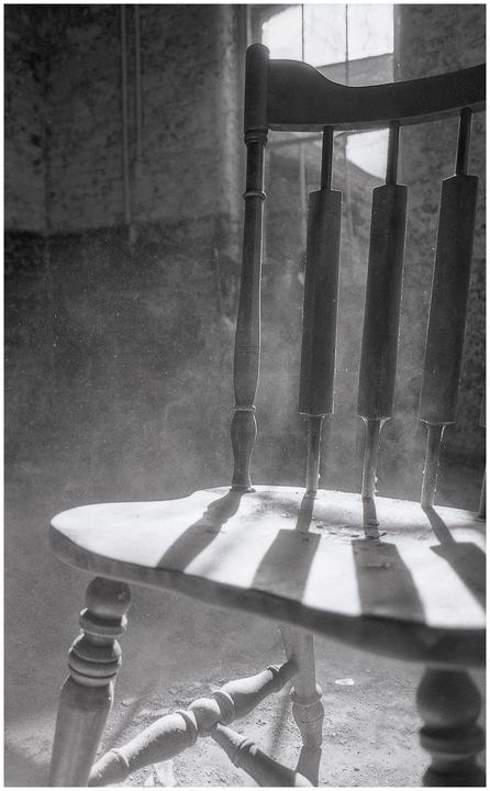 Sunlight streams through a window, illuminating dust motes and casting shadows from a wooden chair.