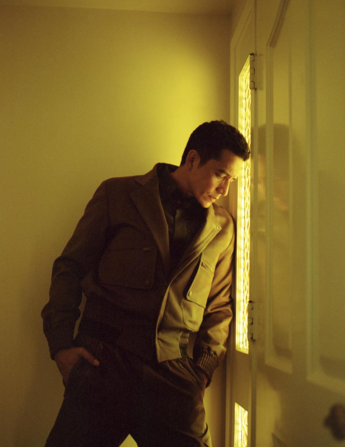 A man in a jacket leans against a door with a glowing panel.