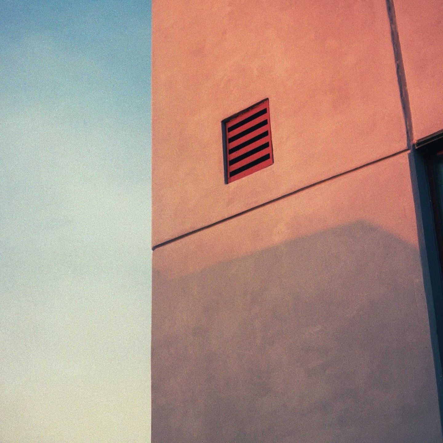 A building facade with a red vent is illuminated by the setting sun against a clear sky.