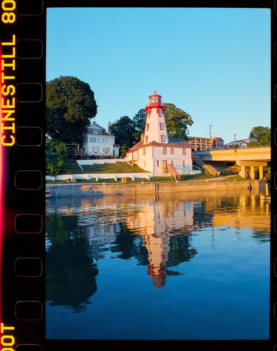 A white lighthouse with a red top stands beside a body of water, reflecting in the calm surface.
