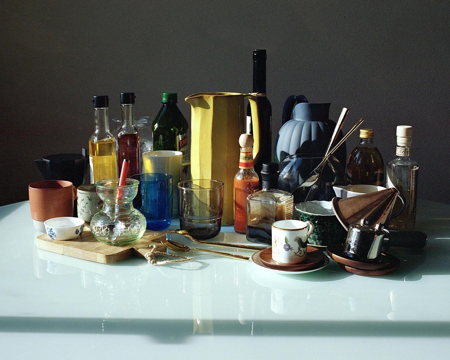 A collection of kitchen items, including bottles, glasses, and cups, is arranged on a reflective surface.