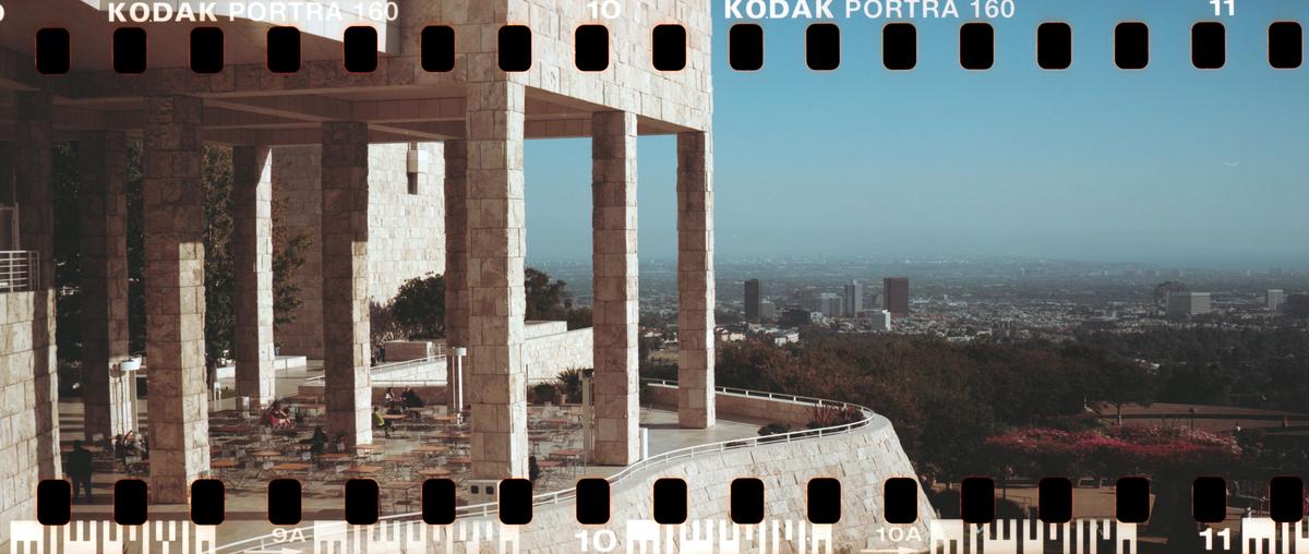 A large stone building with columns overlooks a city and hills under a hazy sky.