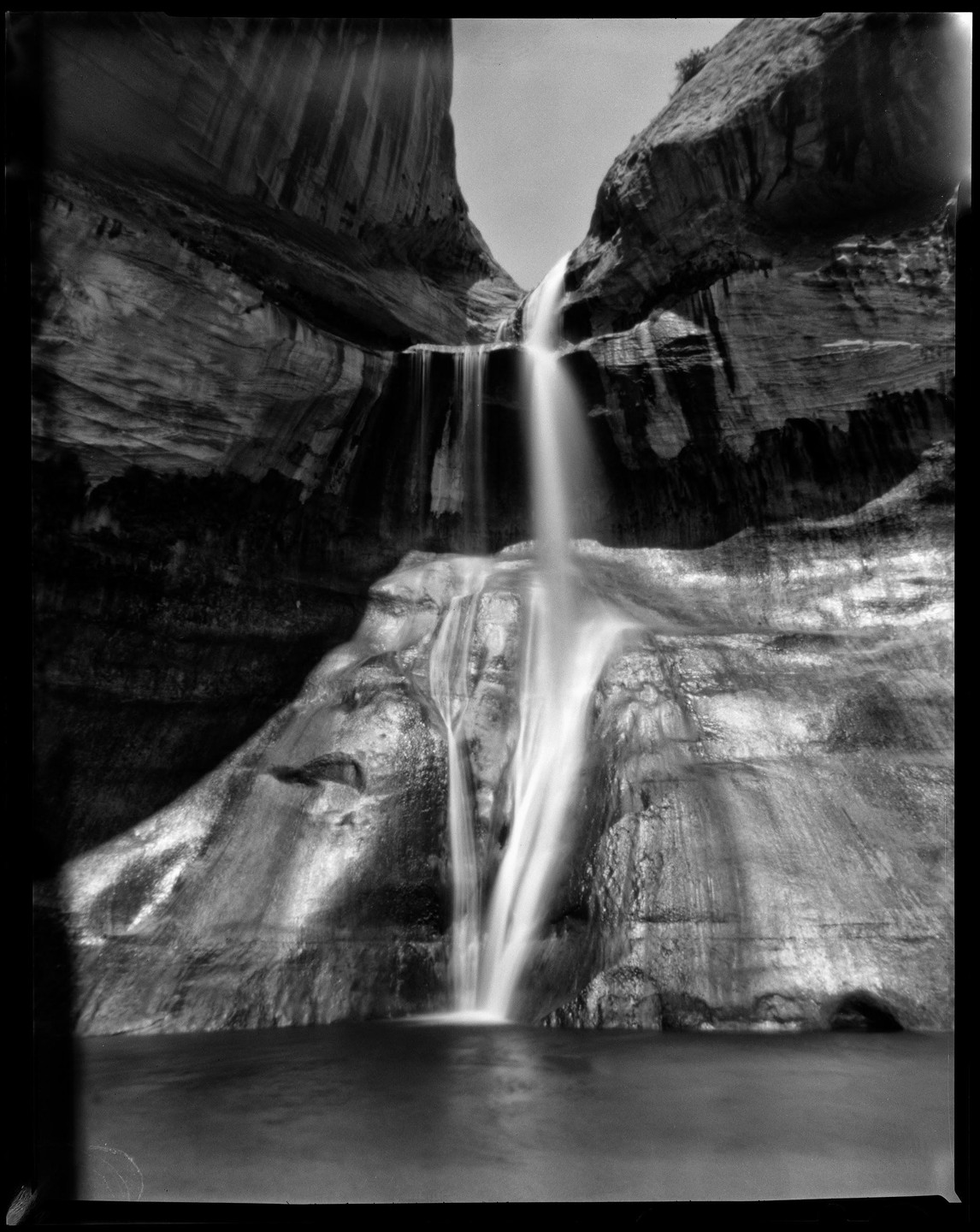 A waterfall cascades down a rocky canyon into a pool of water.